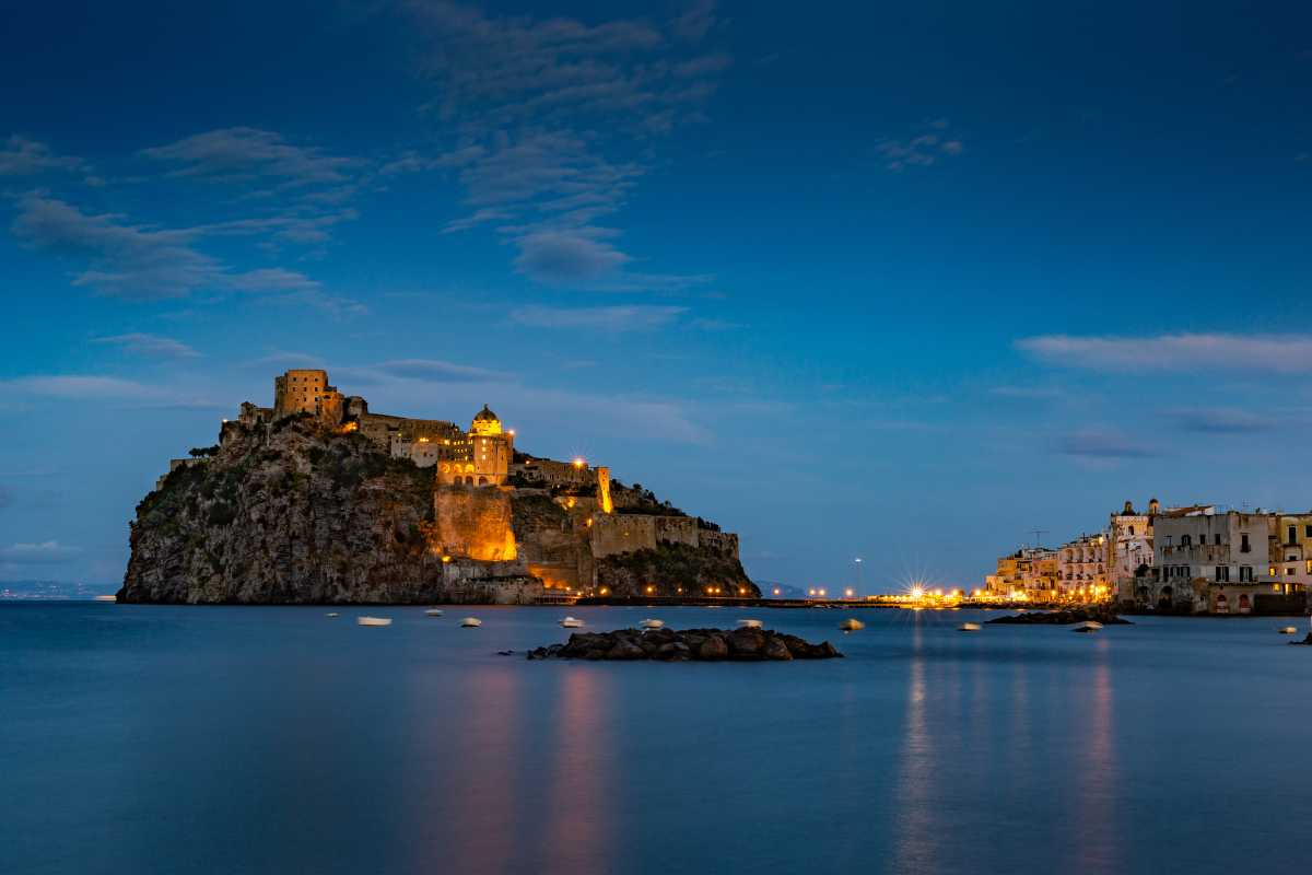 Panorama festoso di Ischia durante una sagra popolare: luci, gente in abiti tipici, bancarelle di prodotti locali con il Castello Aragonese sullo sfondo